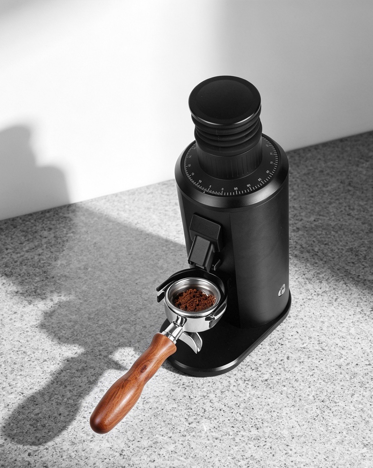 Black espresso grinder with a portafilter positioned beneath the coffee chute